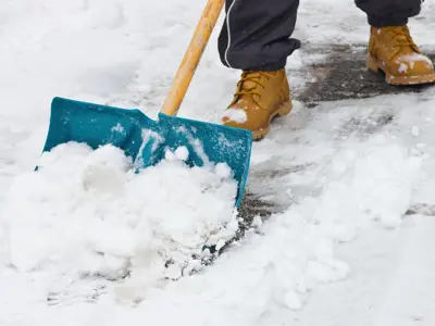 Snow shovel being used to clear snow off of a sidewalk.