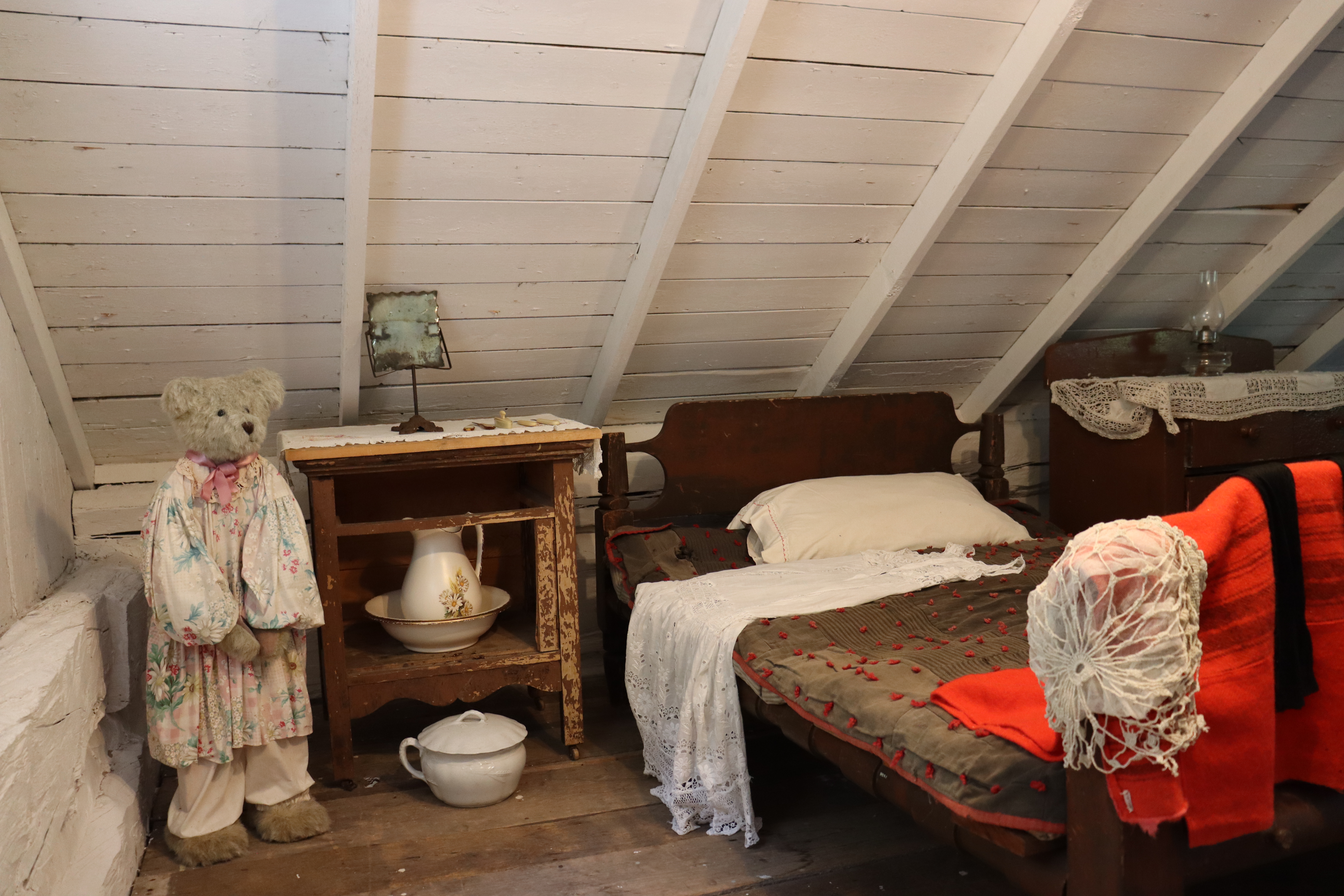 Interior of a heritage home showing a vintage bed setup with cozy quilts and historical furnishings.