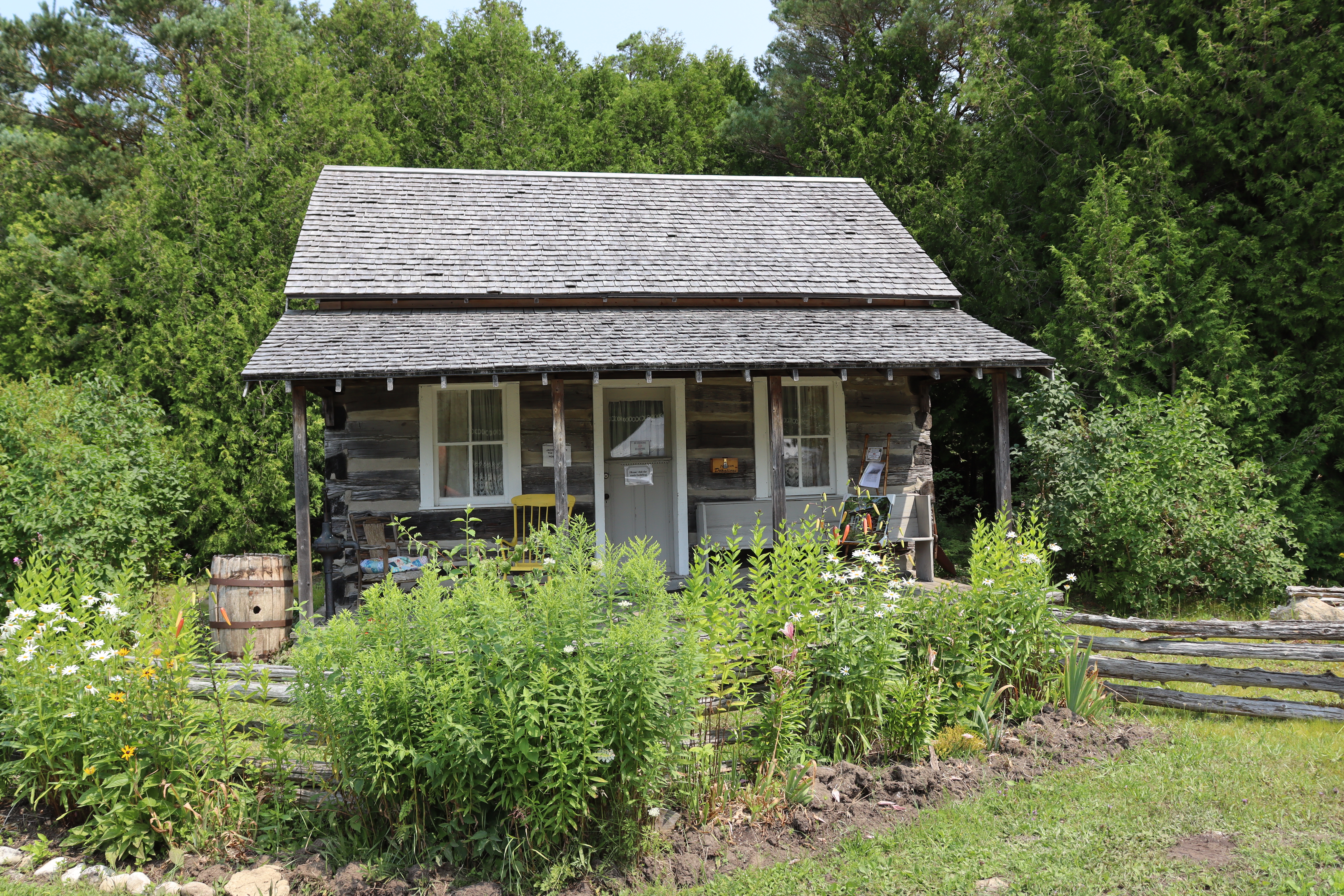 A quaint log cabin surrounded by greenery and tall trees, evoking pioneer homesteading.