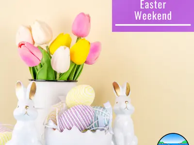 Decorative yellow and pink tulips in a vase with white ceramic rabbit statues in front on a table. 