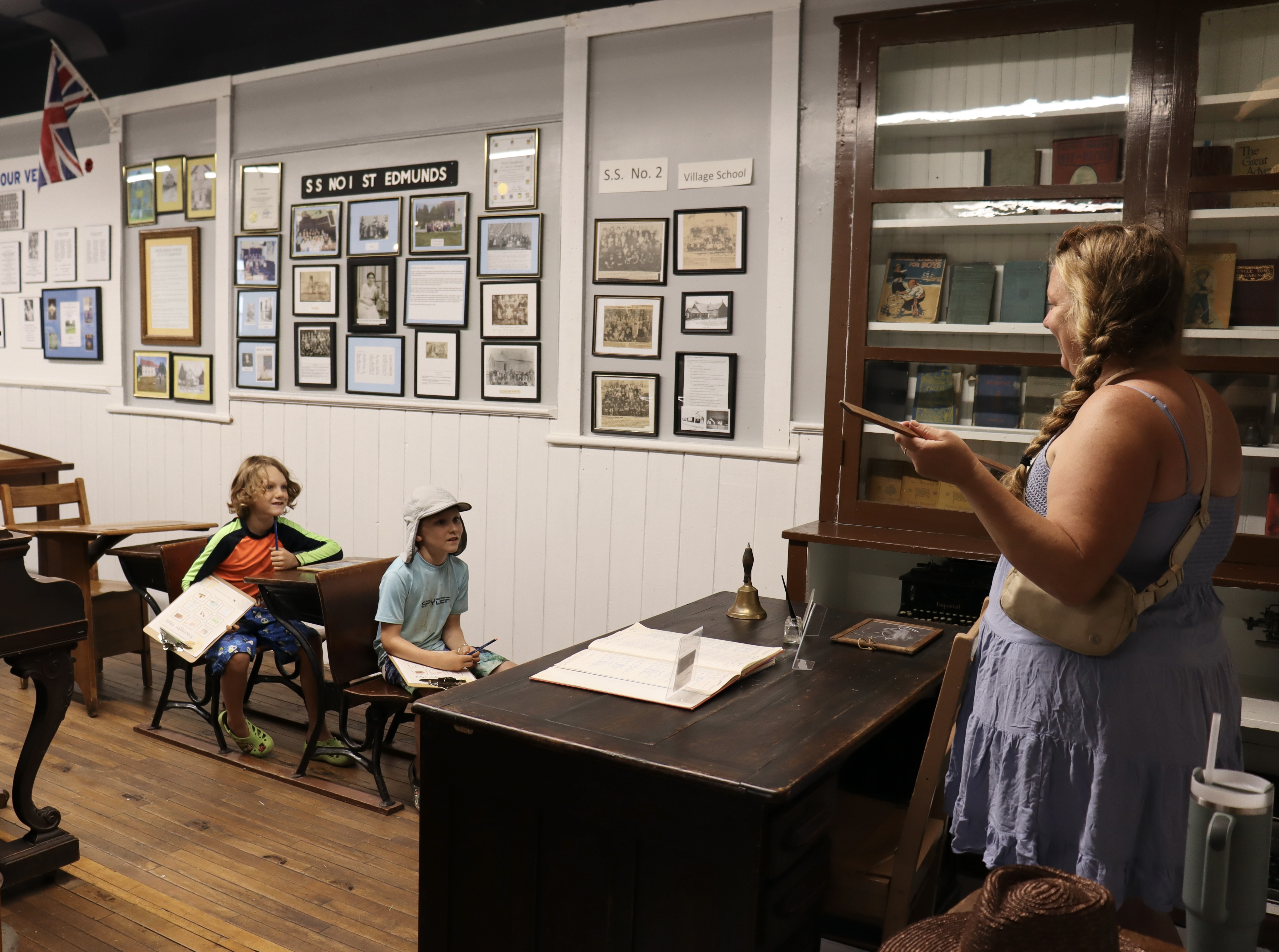 Visitors engaging in a hands-on activity at old-fashioned school desks inside a heritage schoolhouse.