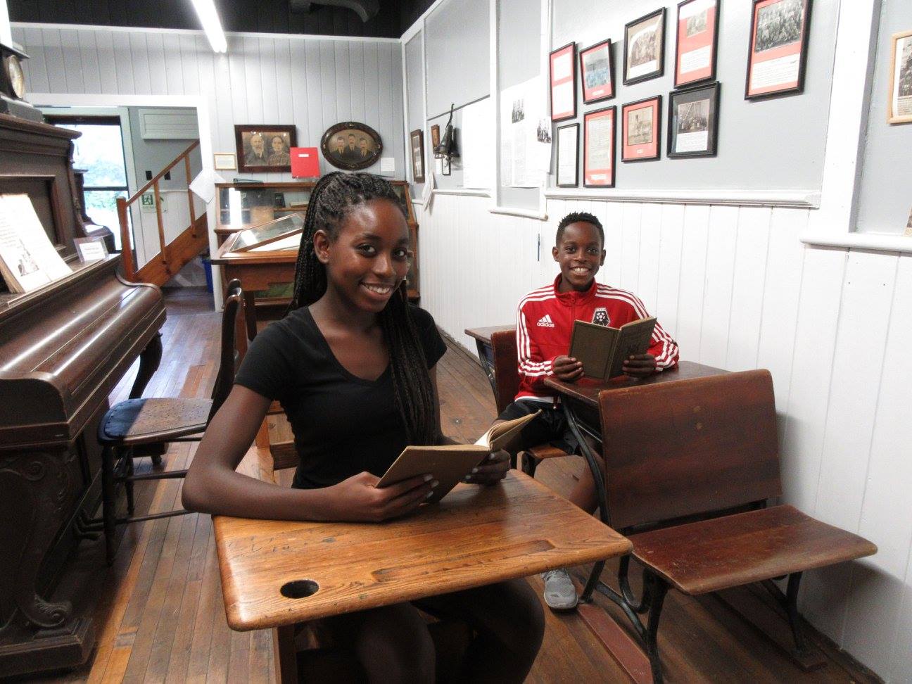 Visitors engaging in a hands-on activity at old-fashioned school desks inside a heritage schoolhouse.